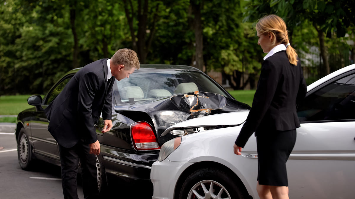 Liikluskindlustuse uuendamine - valge auto on mustale tagant sisse sõitnud, ärimees ja ärinaine uurivad õnnetuse asjaolusid