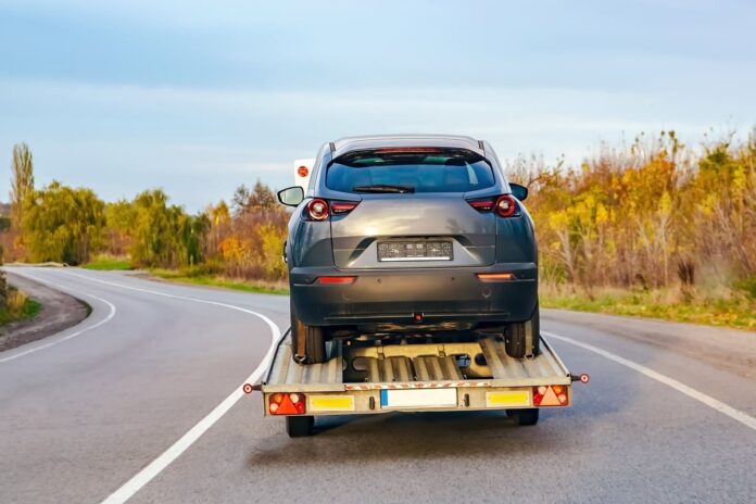 Liikluskindlustuse autoabi mais - tumehall sõiduauto puksiiril läbi looduse liikumas