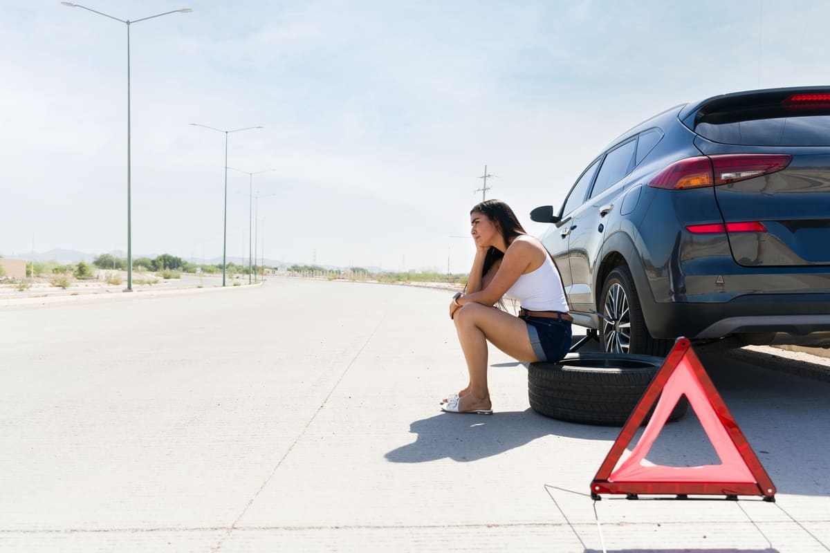Autoabi liikluskindlustusele mais - naine rehvi peal istumas ja abi ootamas